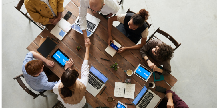 Ariel view of people sitting around a table with laptops and notepads. Two of them shaking hands